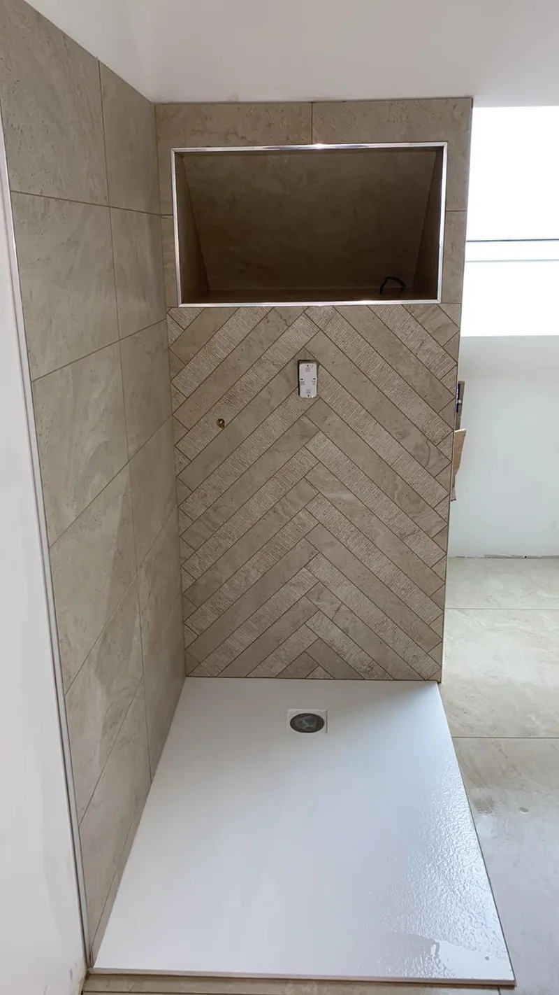 Douche a l'italienne terminee : mur du fond en carrelage effet travertin pose en chevron, grande niche integree bordee d'un profile chrome, mur lateral en grand format effet travertin, receveur extra-plat blanc