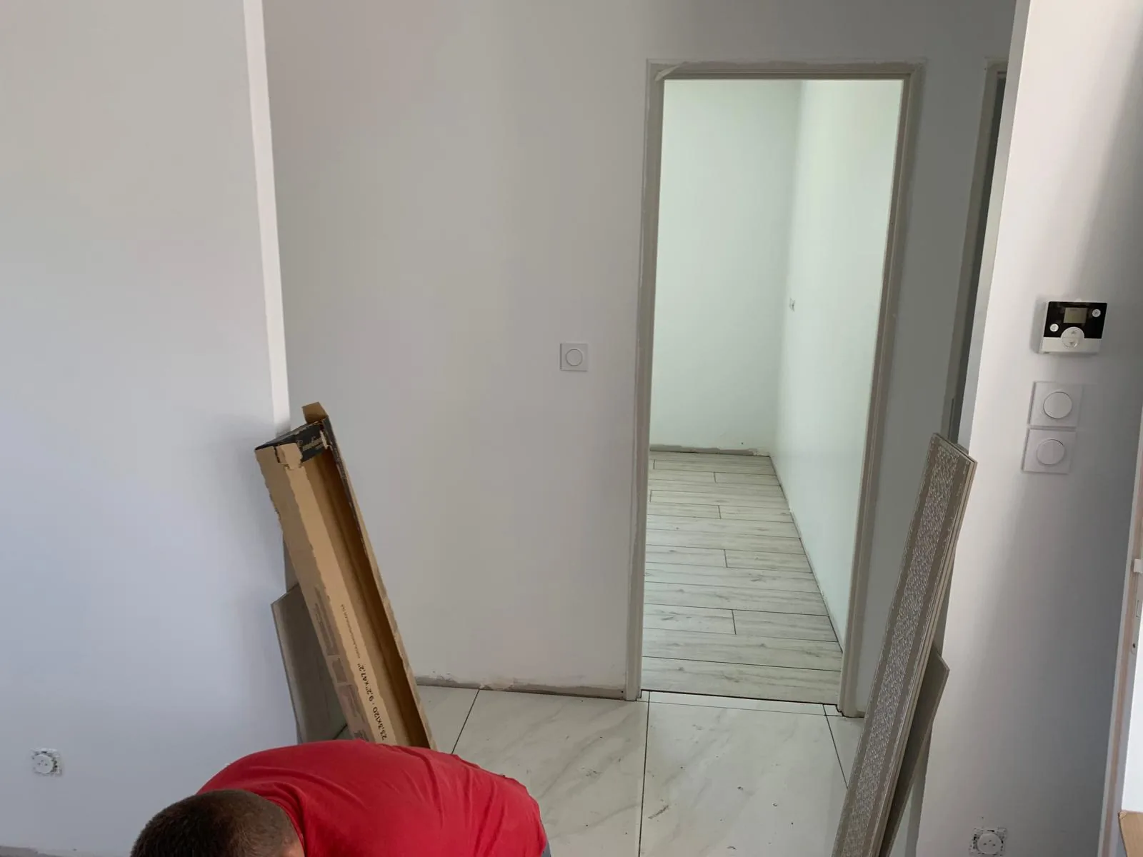 Degagement au sol carrele en grand format effet marbre blanc, avec une ouverture sur une piece au sol en carrelage imitation bois clair