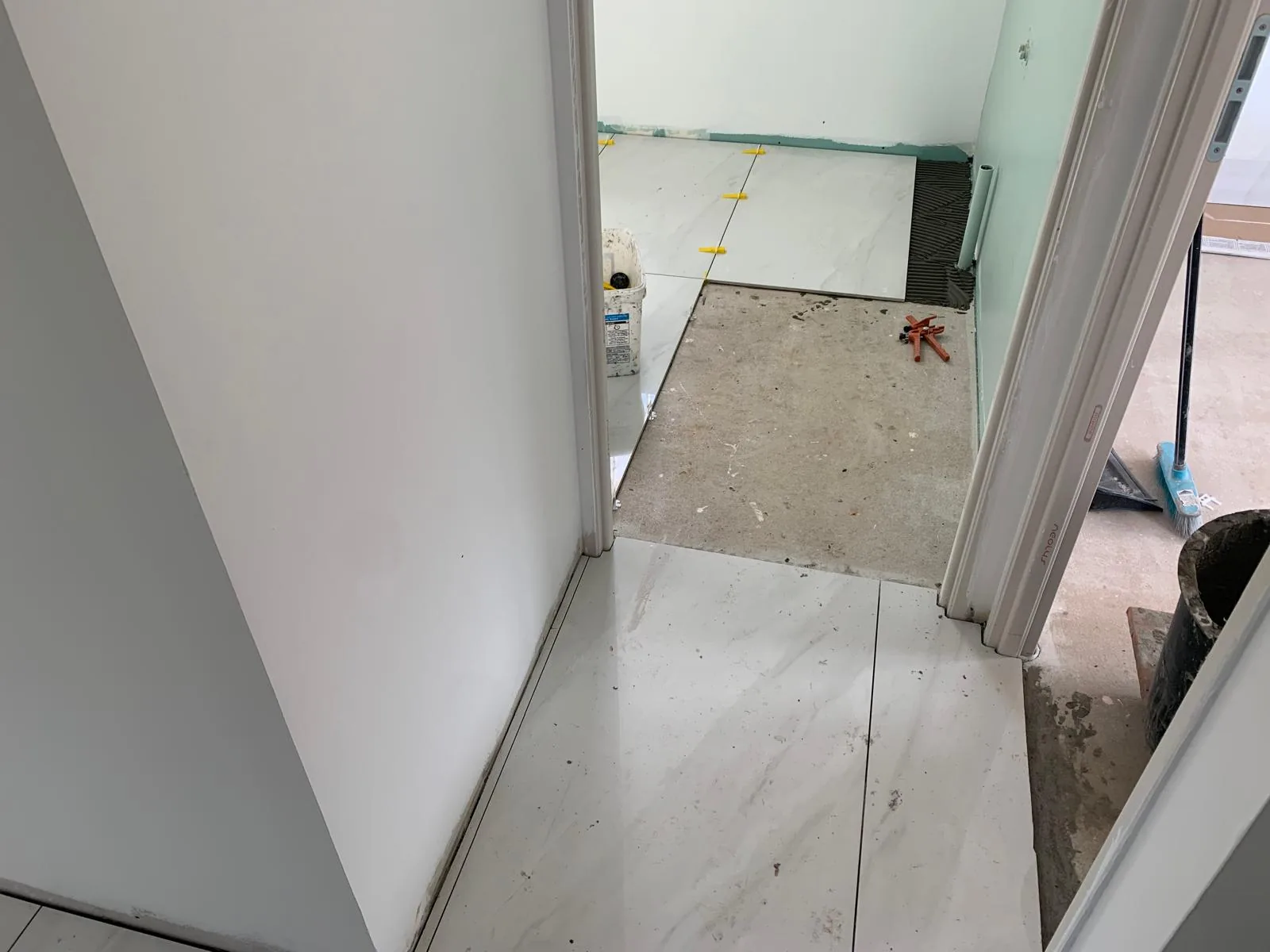 Couloir au sol en carrelage grand format effet marbre blanc, ouvrant sur une piece dont le sol est en cours de pose avec croisillons autonivelants jaunes