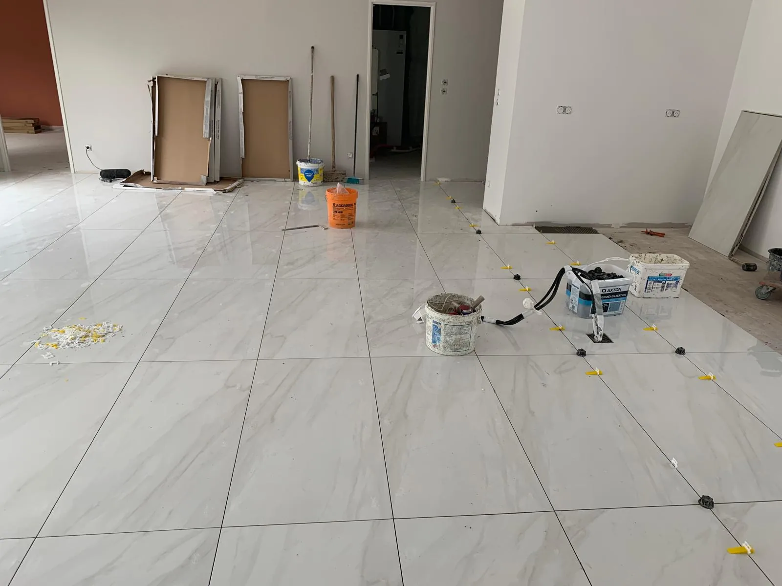 Pièce en chantier au sol carrelé grand format effet marbre blanc, avec seaux et panneaux entreposés le long des murs