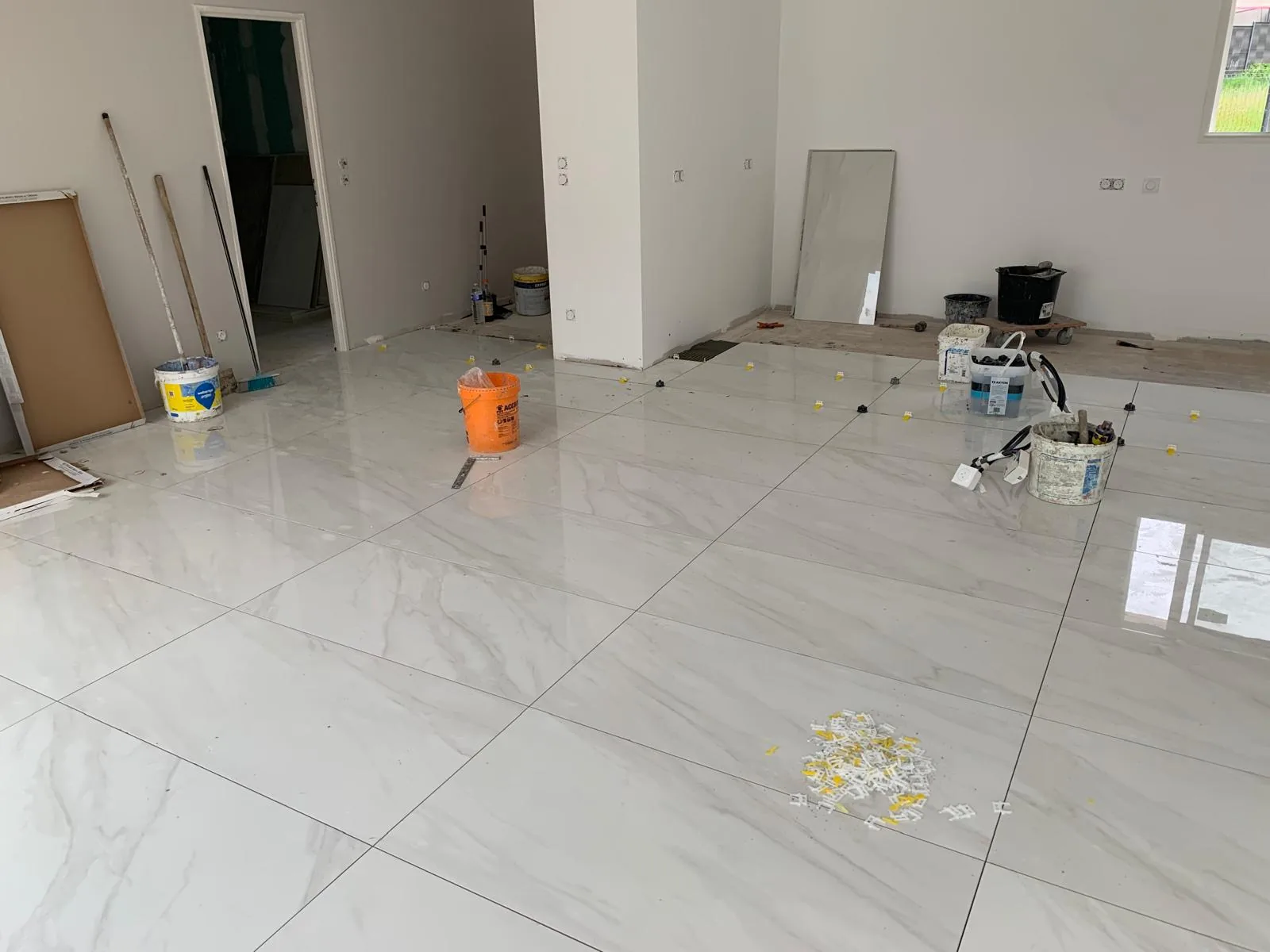 Sol en carrelage grand format effet marbre blanc dans une pièce en chantier avec une ouverture vers une autre pièce et des matériaux entreposés
