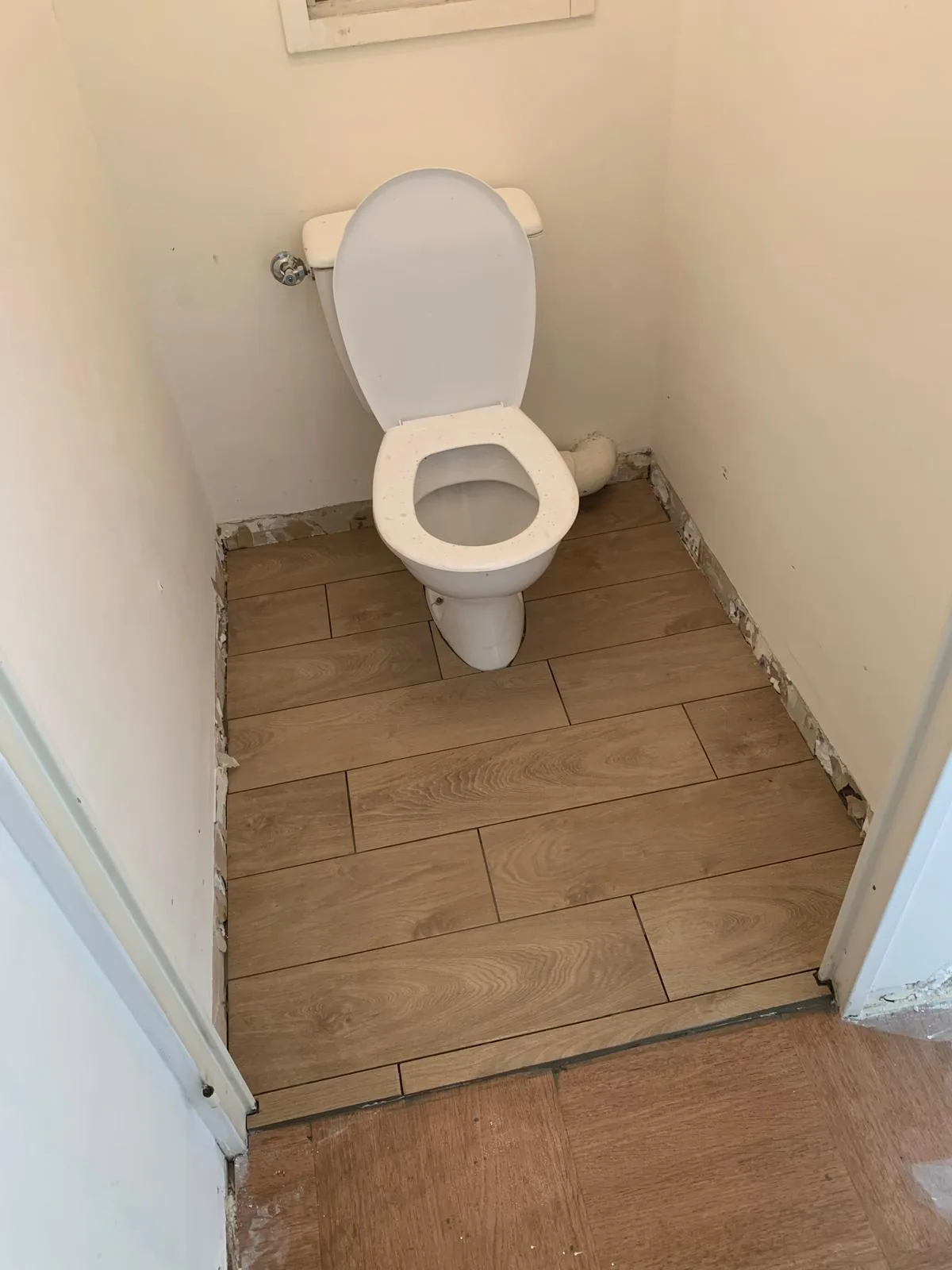 WC avec un sol en carrelage imitation bois clair posé en lames à joints décalés, autour d'une cuvette blanche