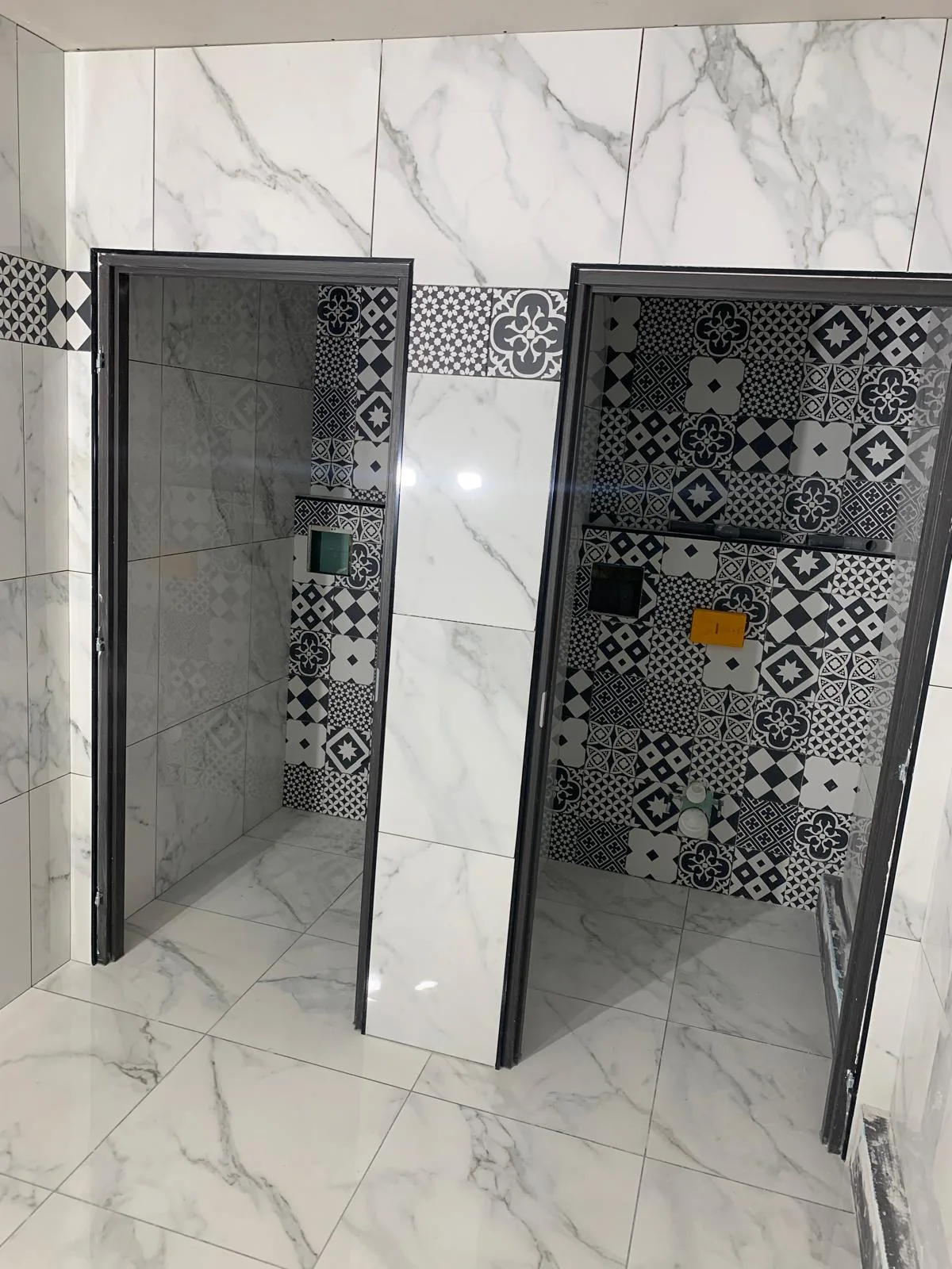 Cabines de douche aux murs en faïence grand format effet marbre blanc, avec fond en carreaux à motifs noir et blanc et parois vitrées à profilés sombres