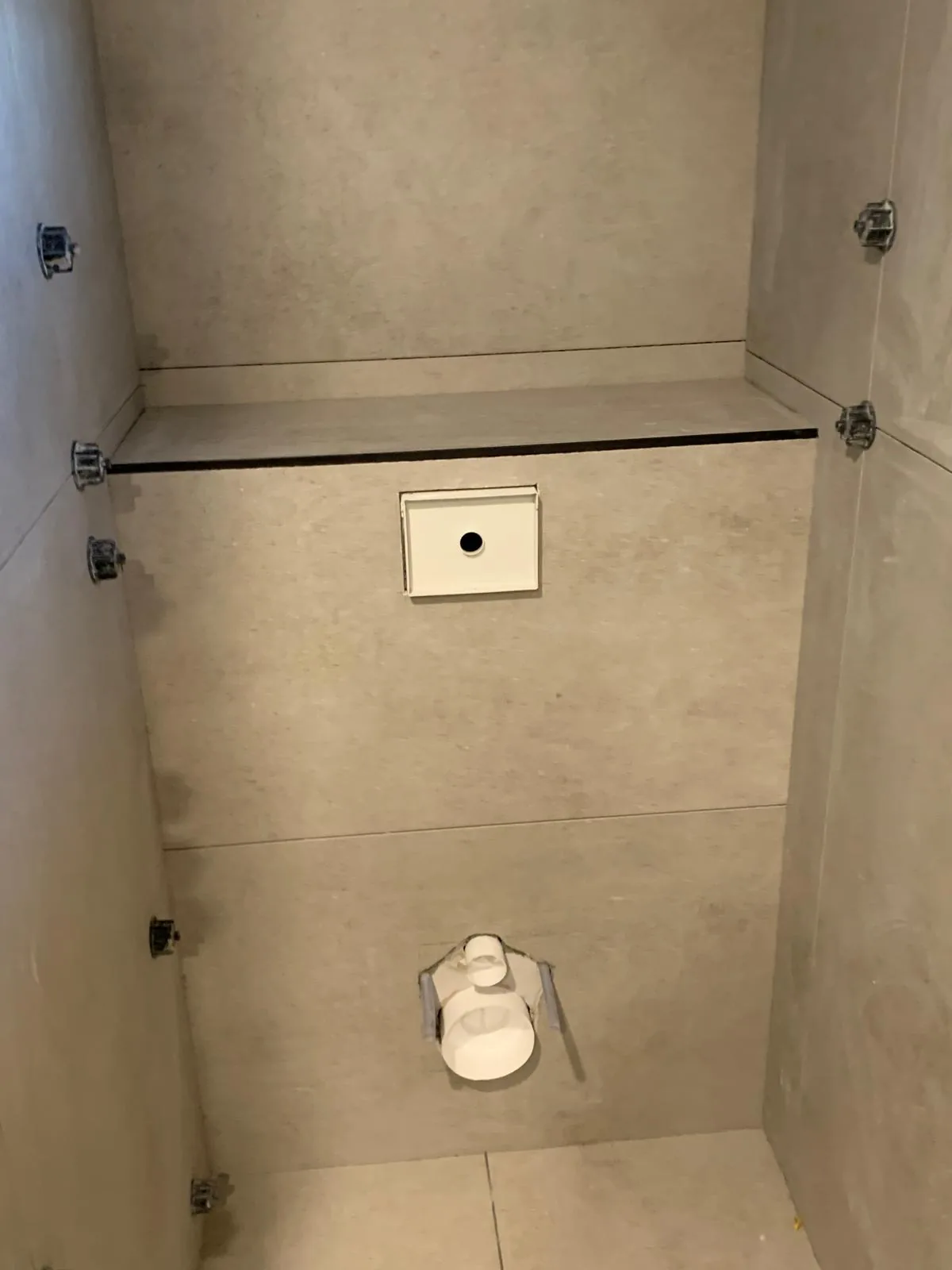 Coffrage de WC suspendu habillé de carrelage grand format beige, avec la réservation de la plaque de commande et les sorties d'évacuation, croisillons autonivelants encore en place