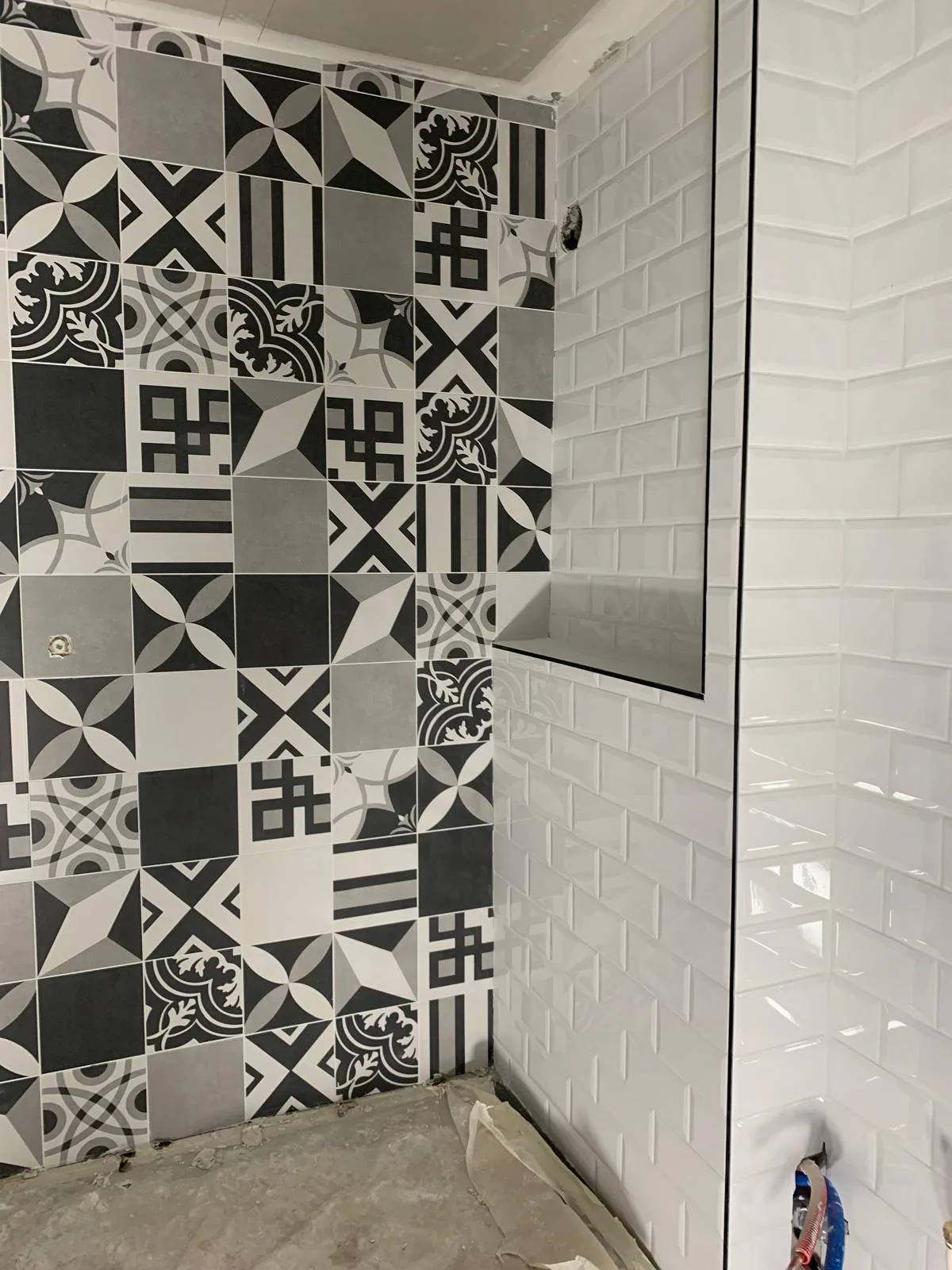 Mur de douche en carreaux type ciment a motifs geometriques noir, blanc et gris, mur adjacent en faience metro blanche biseautee avec tablette integree