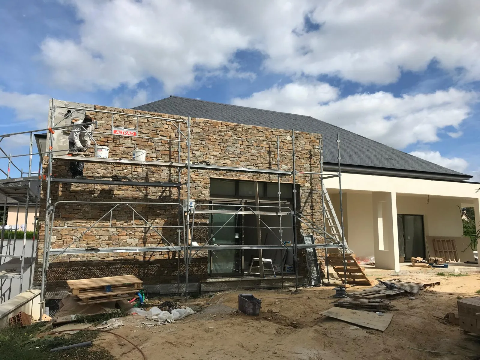 Pignon de maison en cours d'habillage en parement de pierre naturelle beige et ocre, echafaudage devant la facade