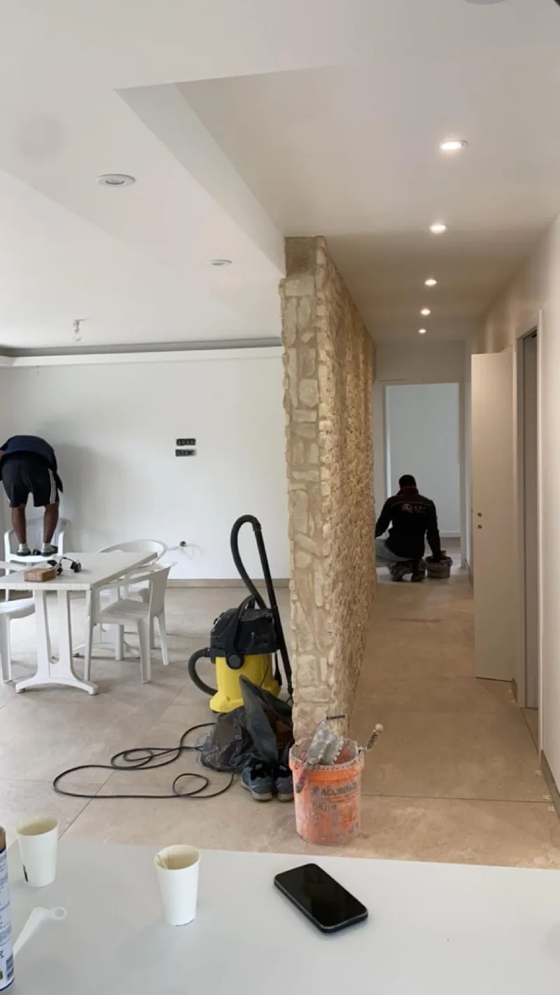 Cloison habillee de pierre de parement beige separant une piece de vie d un couloir, avec sol carrele beige