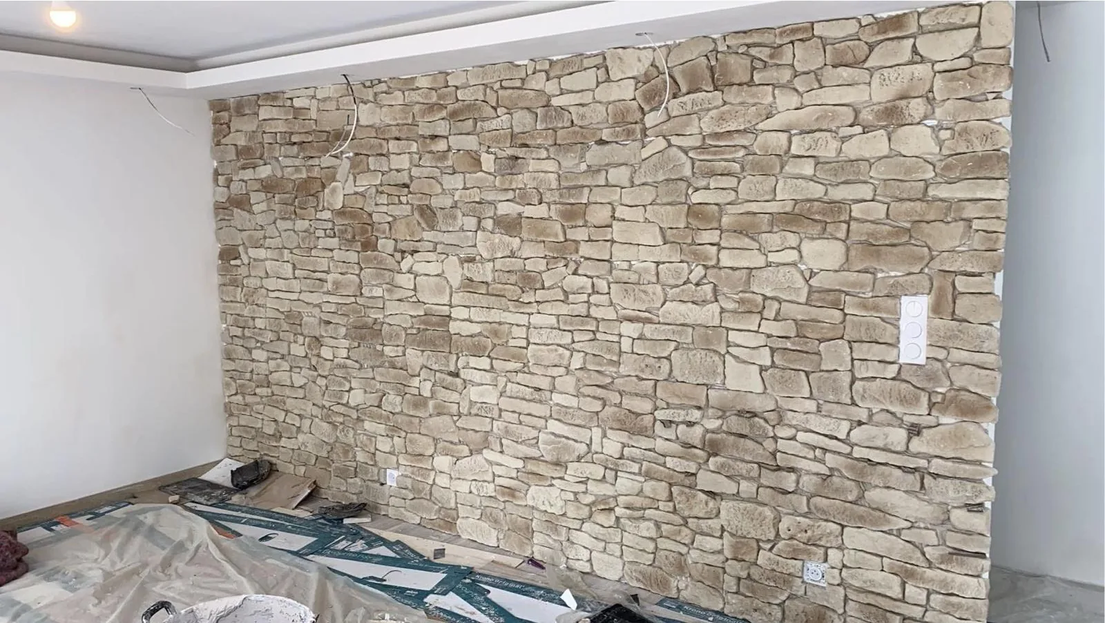 Mur interieur en pierre de parement beige vu en large, montrant l angle de la piece et le plafond