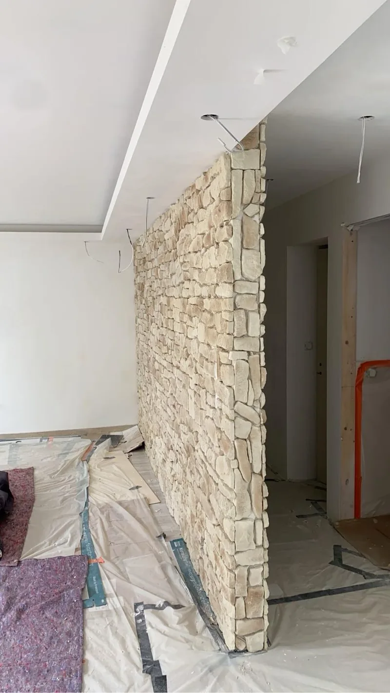 Cloison en pierre de parement beige vue de biais, arete verticale habillee en pierre, piece en chantier