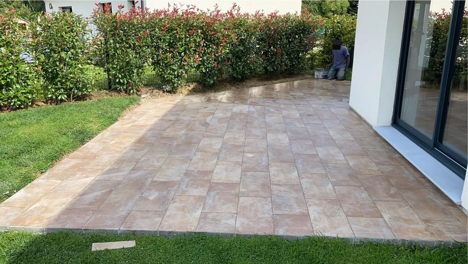 Terrasse carrelee en beige rose le long d une baie vitree, avec pelouse et haie