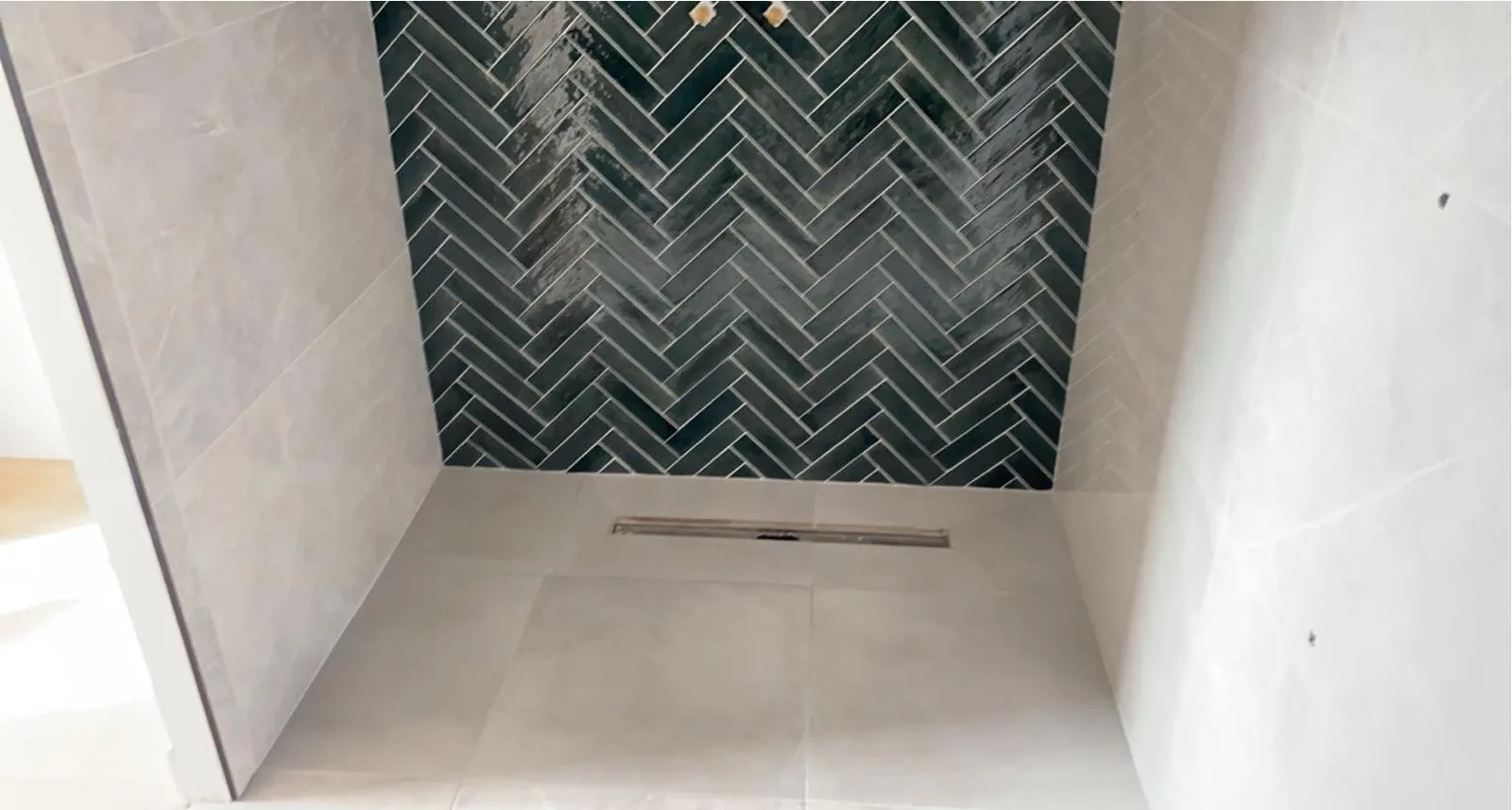 Vue d ensemble d une douche a l italienne avec mur du fond vert pose en baton rompu, parois et sol gris clair et caniveau lineaire