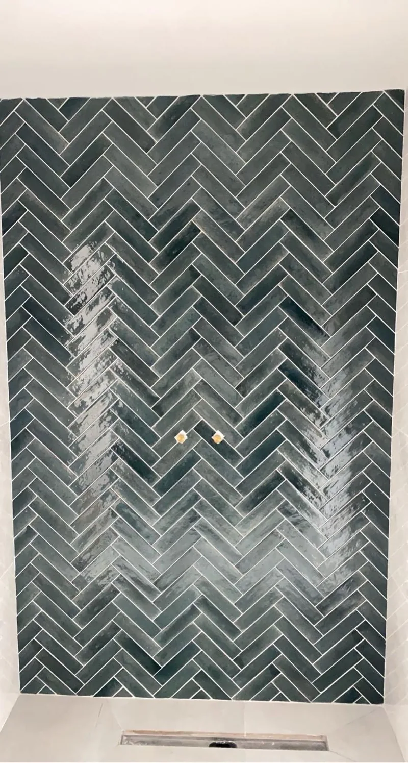 Mur de douche en faience vert fonce brillante posee en baton rompu, encadree de carrelage grand format clair, avec caniveau lineaire au sol