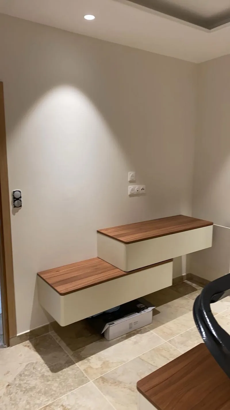 Sol carrele de grands carreaux aspect travertin beige, sous un meuble suspendu a plateaux bois eclaire par un spot mural
