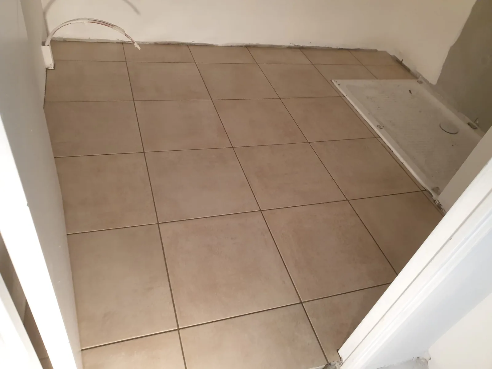 Petite piece au sol recouvert de carreaux beiges unis de grand format poses droit. A droite, un receveur de douche blanc encastre. Une gaine sort du mur en haut a gauche.