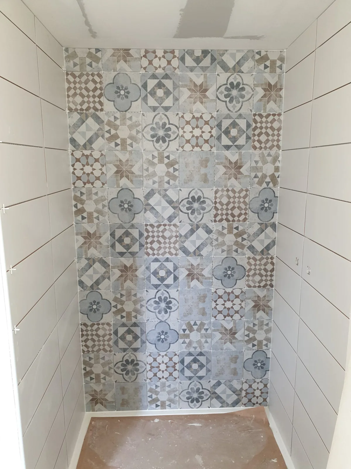 Niche etroite dont le mur du fond est entierement habille de carreaux a motifs geometriques bleus, gris et bruns facon carreaux de ciment, en patchwork. Les murs lateraux sont habilles de faience blanche allongee posee droit.
