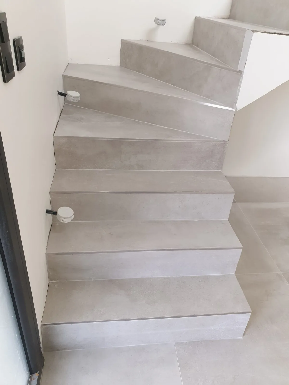 Escalier intérieur carrelé en gris clair effet béton, avec marches balancées, nez de marche en aluminium et sol assorti