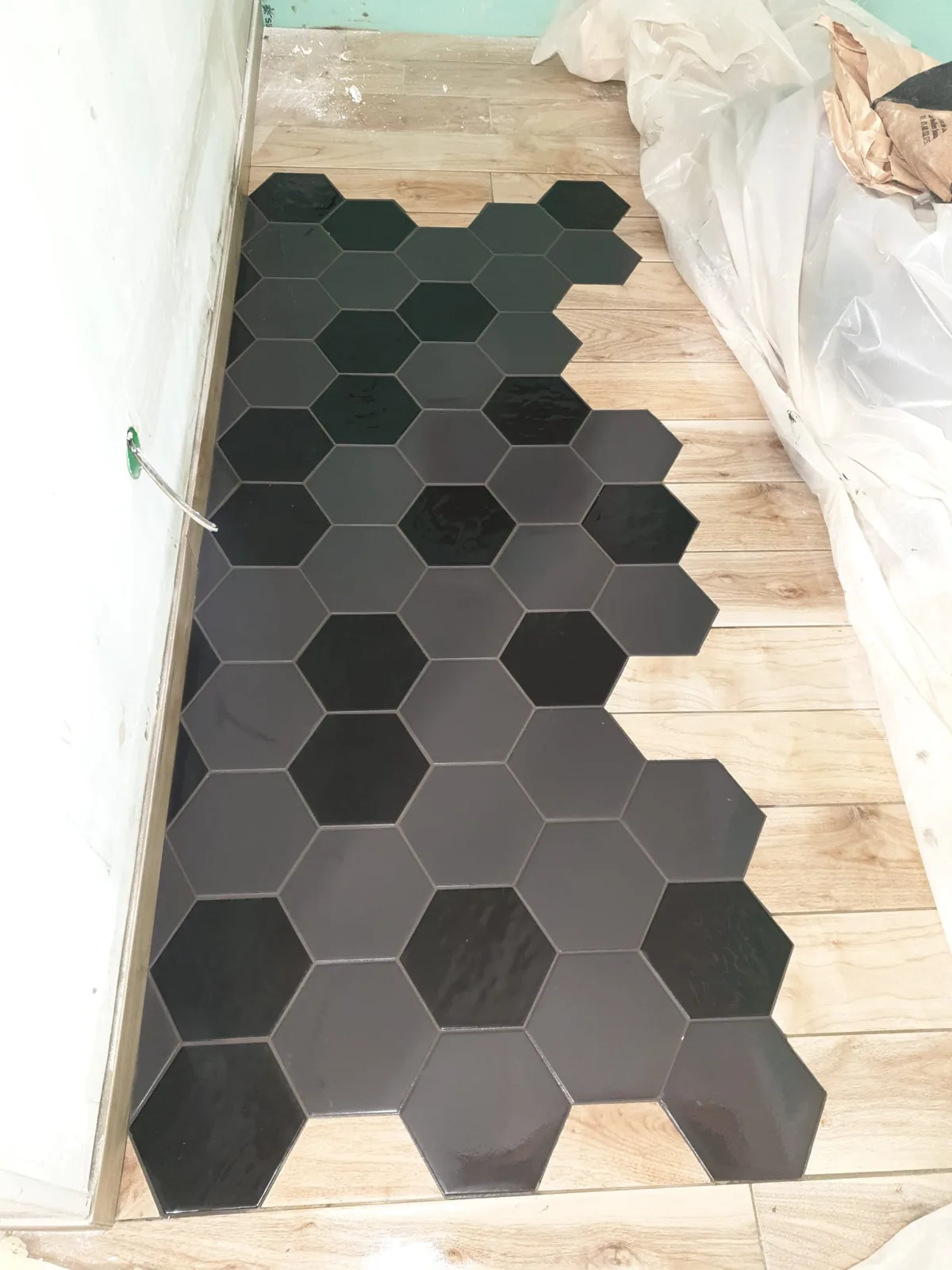 Sol intérieur montrant une transition imbriquée entre un carrelage hexagonal noir et un carrelage imitation bois clair