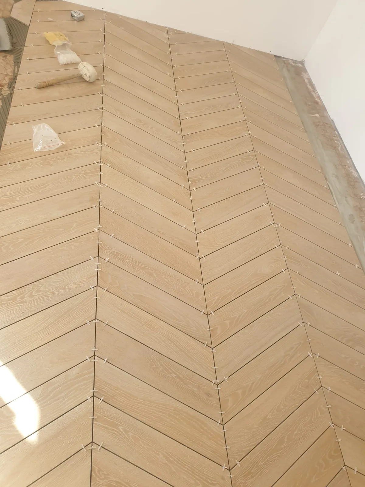 Sol en carrelage imitation bois posé en chevron, en cours de pose avec croisillons et outils