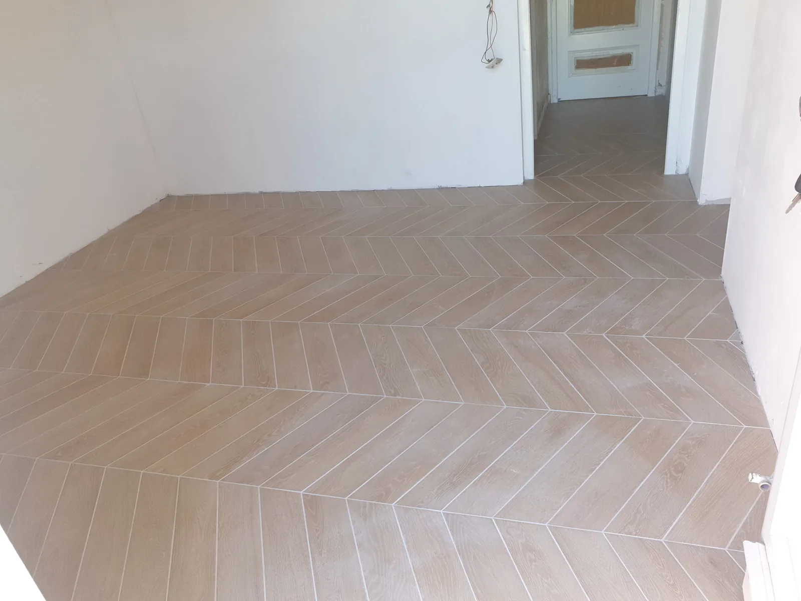 Pièce vide avec un sol en carrelage imitation bois posé en chevron, se prolongeant dans un couloir