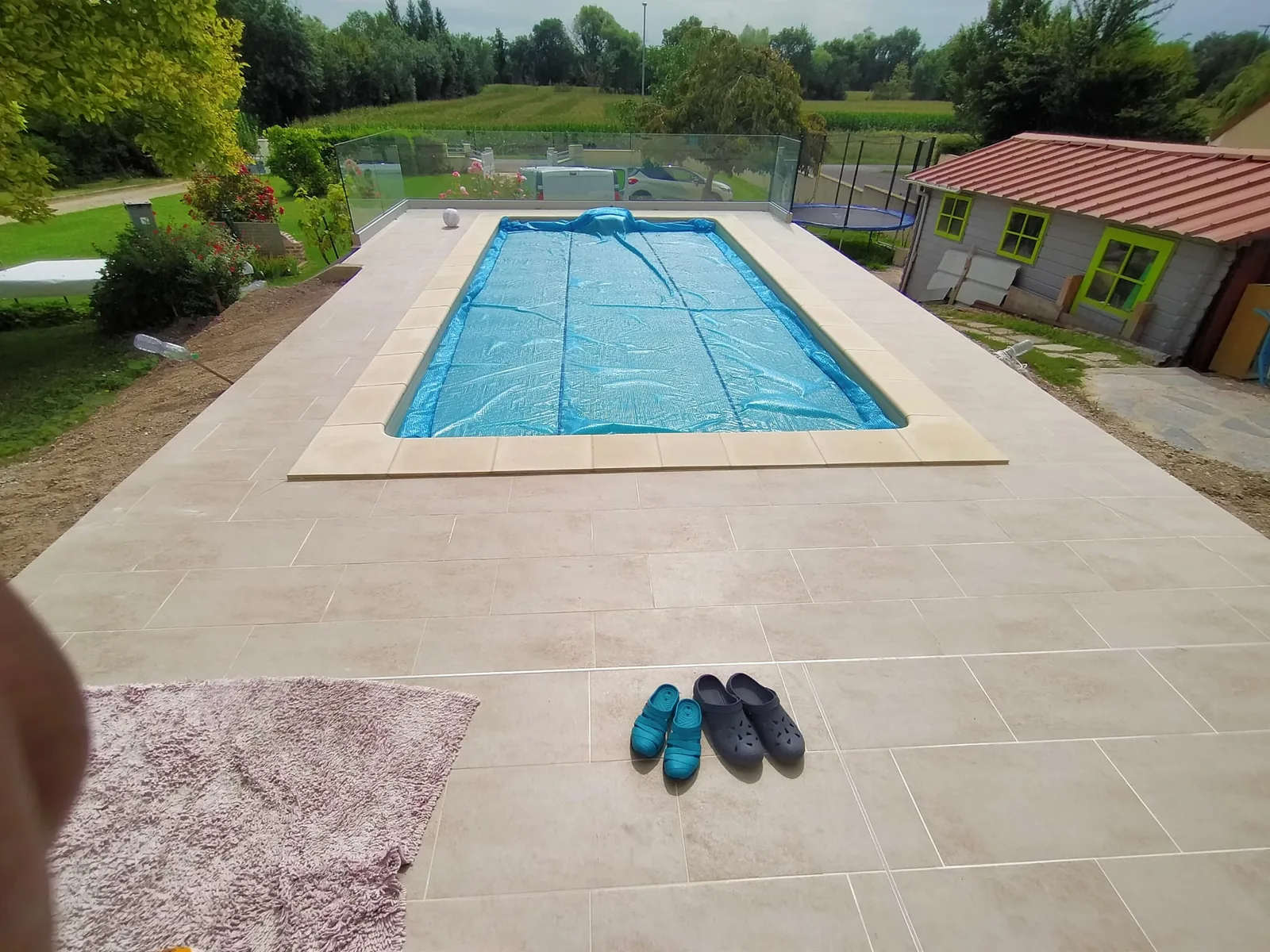 Piscine rectangulaire couverte d'une bâche à bulles, entourée d'une large plage carrelée en dalles claires avec margelles