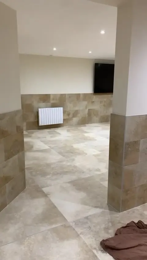 Pièce aux murs blancs avec un soubassement en carrelage aspect pierre beige et un sol grand format assorti, radiateur blanc et poteau habillé